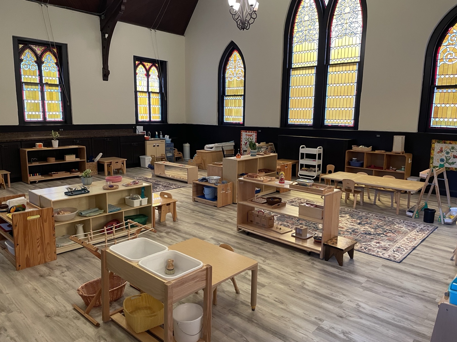 The Starling Toddler classroom — wooden Montessori shelves, child-sized furniture, and warm natural light through stained glass
