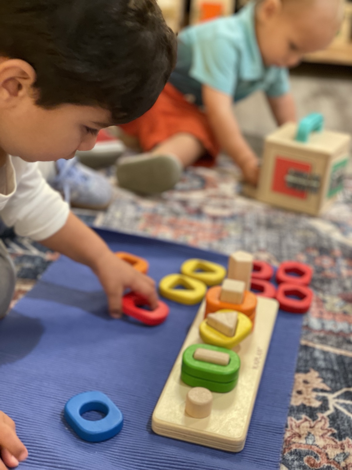 Two Starling children sorting wooden geometric shapes onto a work mat — a sensorial Montessori material