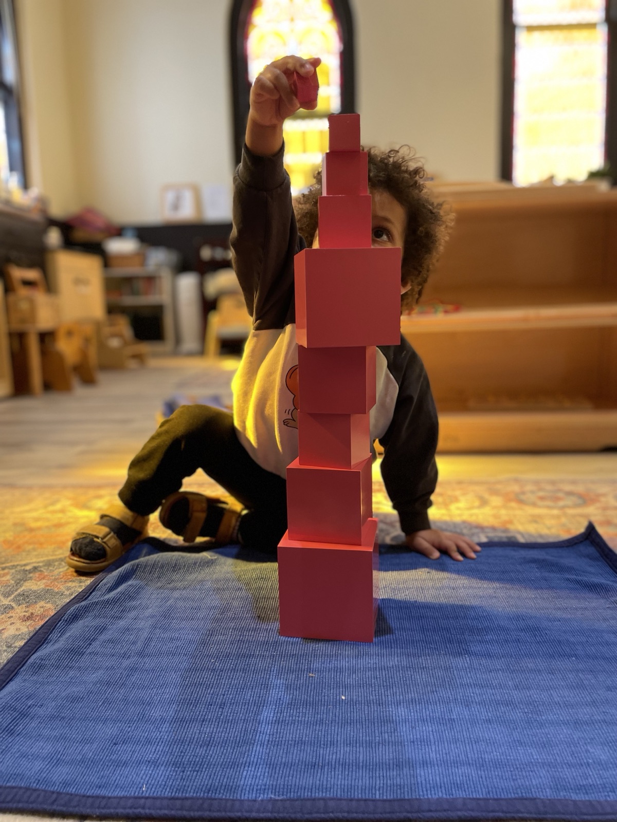 A Starling child carefully placing the top cube of the Pink Tower — a foundational Montessori sensorial material